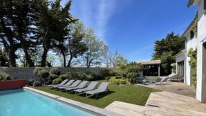 Un área de piscina moderna al aire libre con un muro de piedra, una terraza de madera y un porche cubierto.
