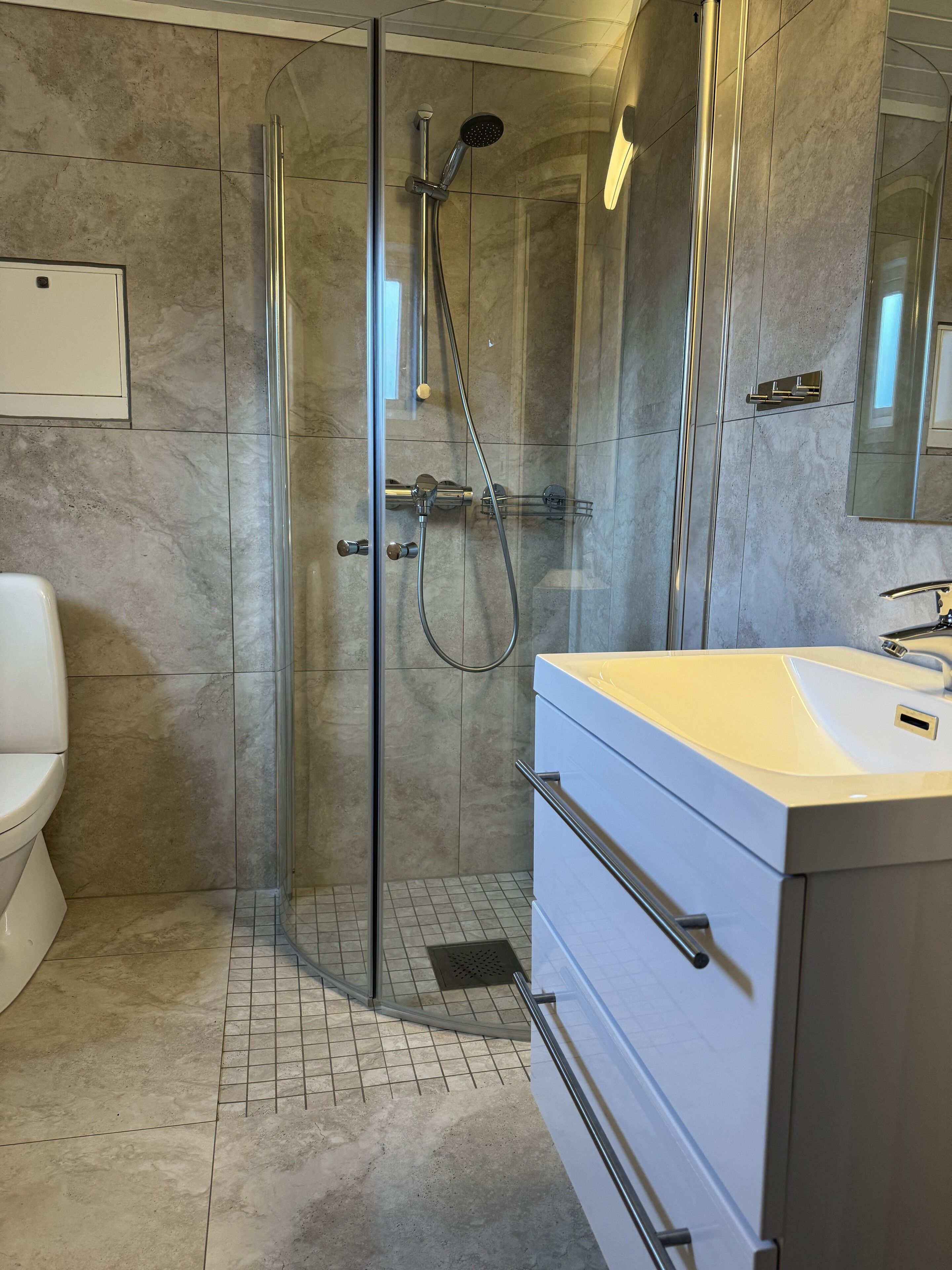 Ein modernes Badezimmer mit einer Glasdusche, einem weißen Waschbecken und einer Toilette.