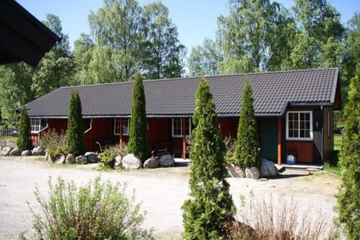 Eine zweistöckige Holzhütte mit dunklem Dach, umgeben von Grünpflanzen und Felsen.