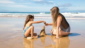 Two people on a sandy beach with ocean waves in the background.
