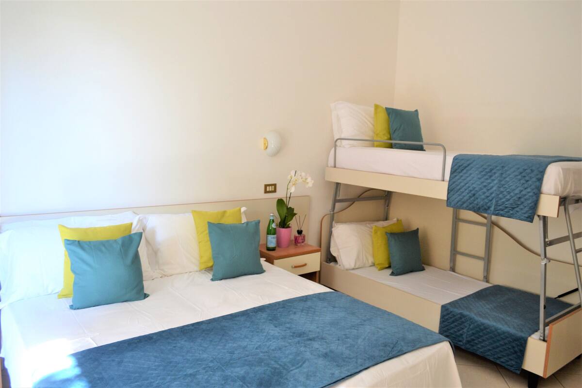A bunk bed room with a white wall, a bedside table with a plant, and a lamp.