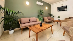 A modern living room with a green accent wall, wicker furniture, and potted plants.
