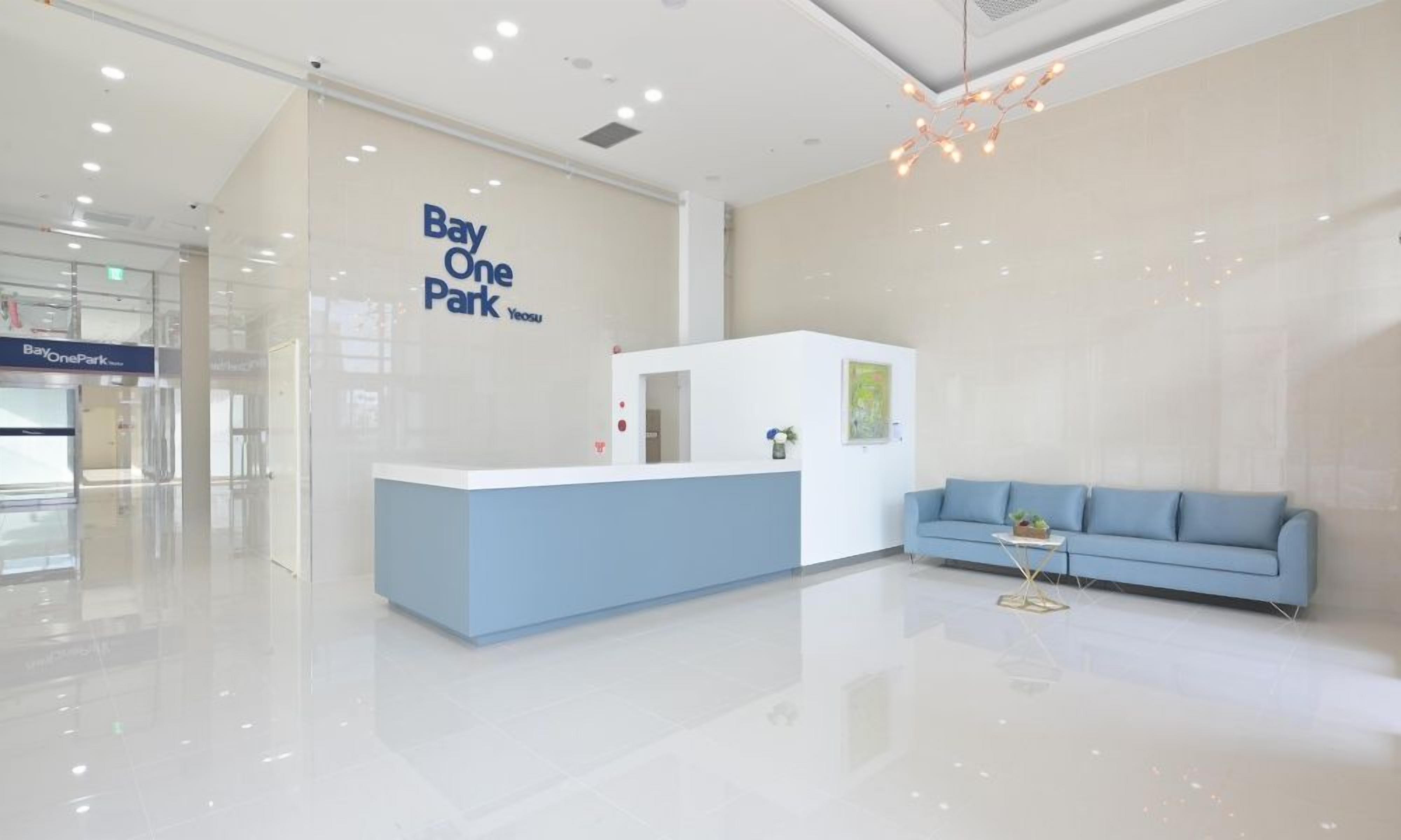 Un área de recepción limpia y moderna con un cartel de Bay One Park, una mesa de recepción y un sofá azul.