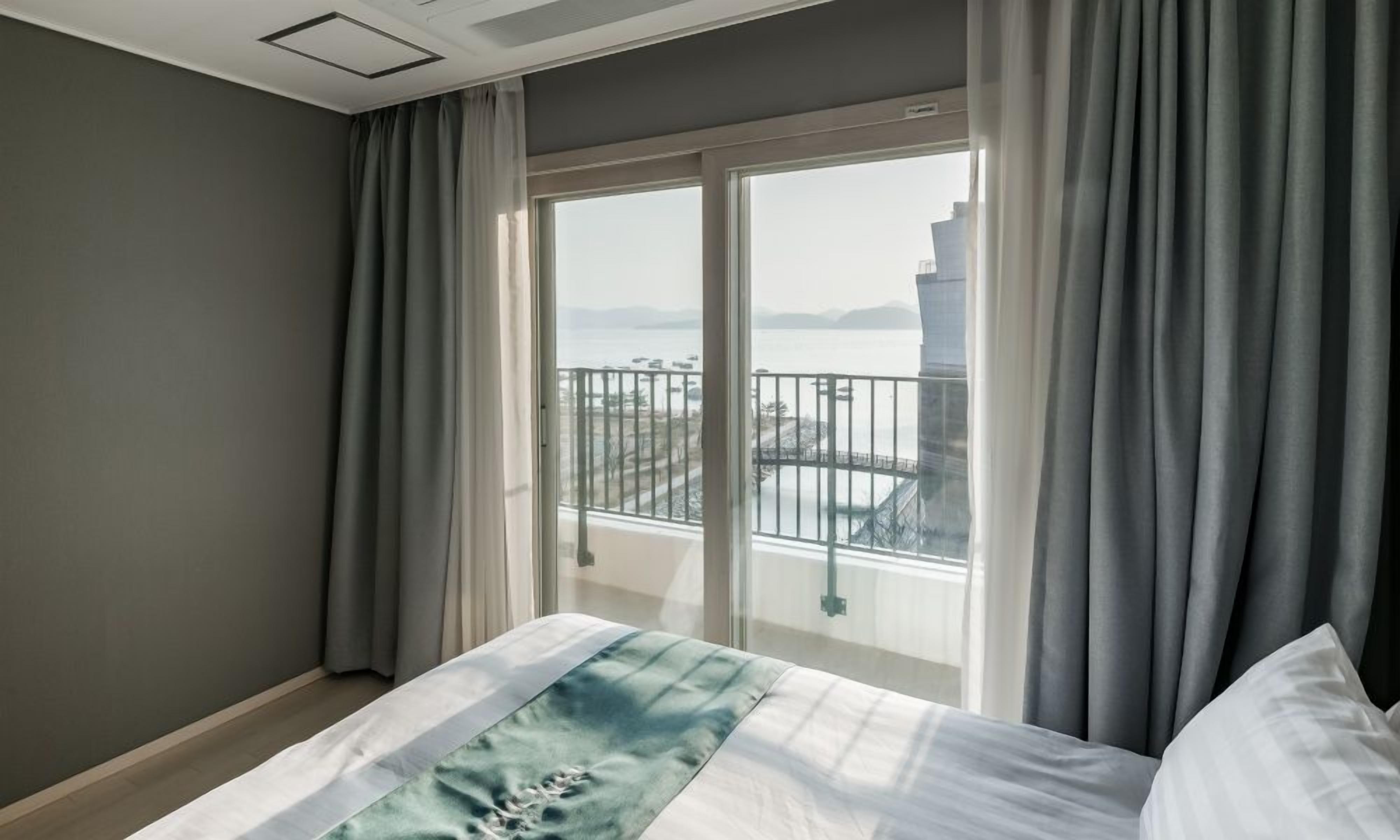 Habitación de hotel con cama, vista a un balcón y un amplio ventanal.