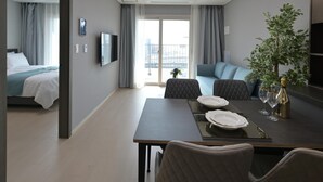Una habitación de hotel moderna con una cama, un área de comedor con una mesa para dos, un sofá y un gran ventanal con cortinas.