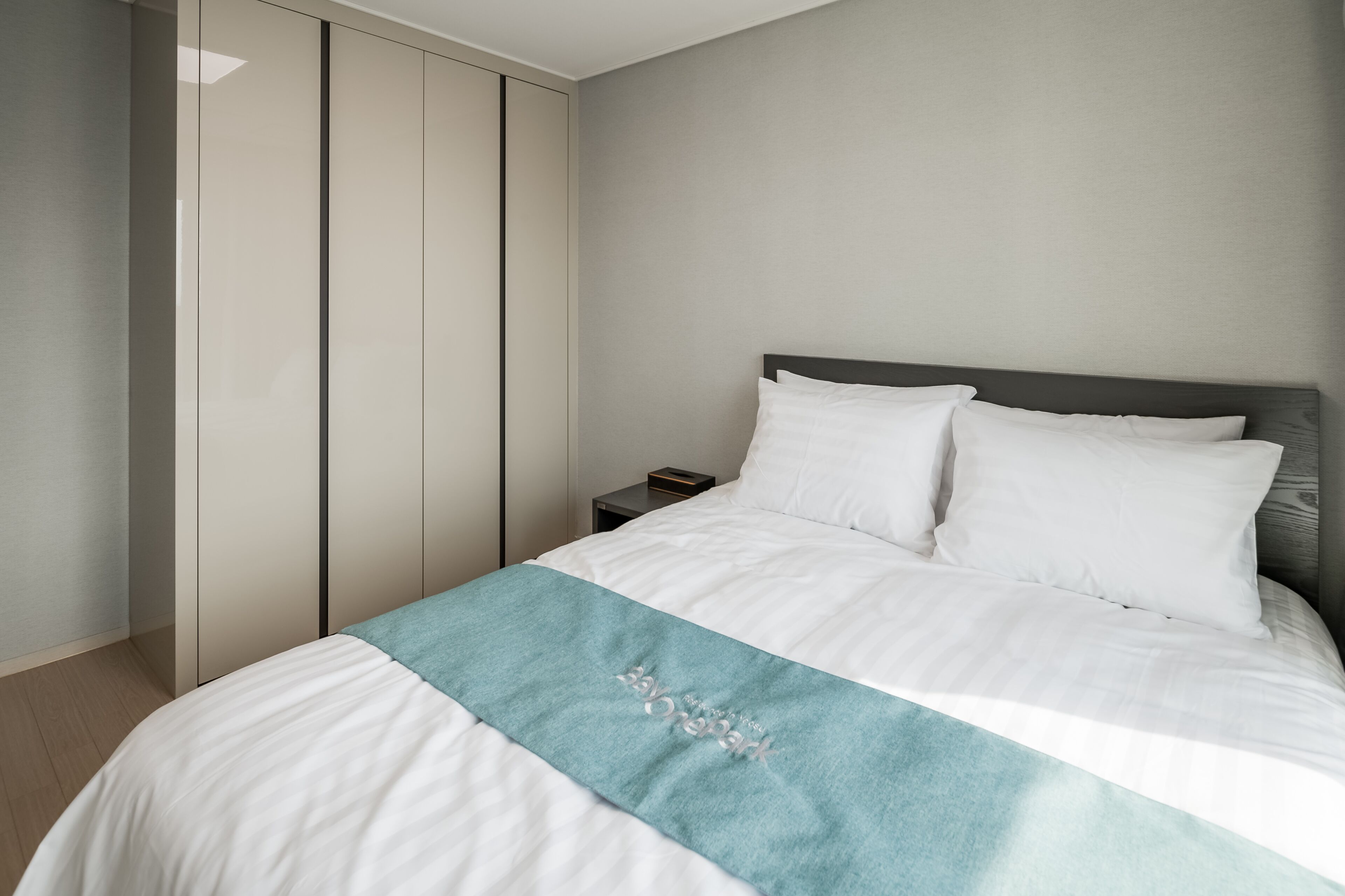 Une chambre à coucher moderne avec un lit, du linge de lit blanc, un plaid turquoise et une table de chevet.