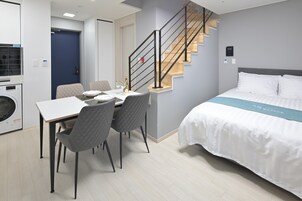 Una habitación de hotel moderna con una cama, una zona de comedor con sillas, una escalera y una lavadora en una esquina.