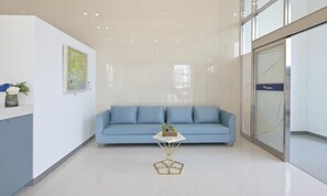 A reception area with a blue sofa, a white table with a plant, and a framed artwork on the wall. - BayOne Park (Yeosu)