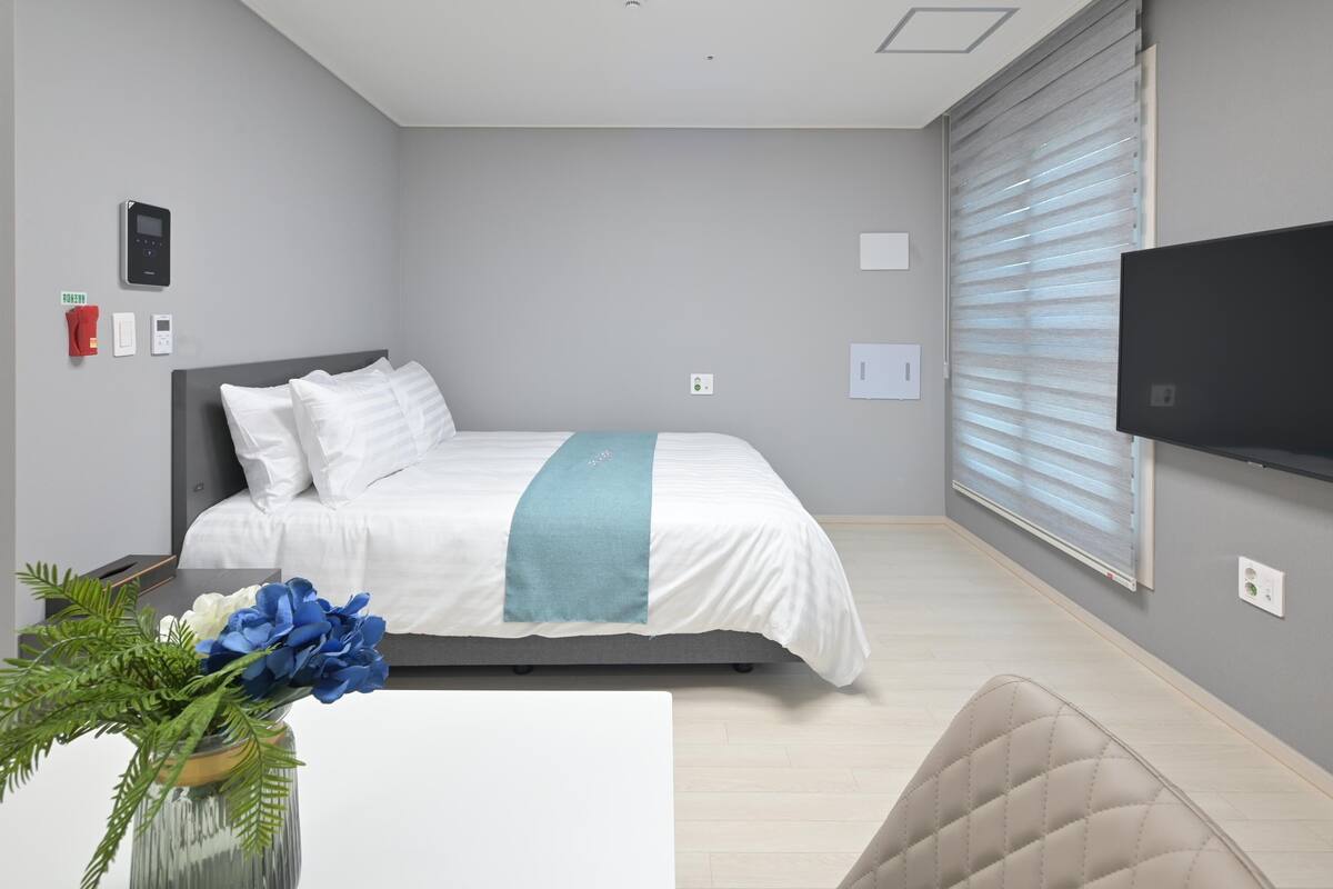 A modern bedroom with a bed, a TV, and a window with blinds.