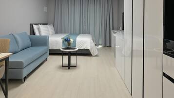 A modern hotel room with a bed, a blue sofa, a small table with a vase, and a TV.