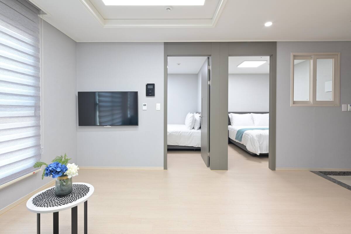 A modern hotel room with a large bed, a flat-screen TV mounted on the wall, and a small table with a vase of flowers.