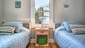 Een slaapkamer met twee bedden, een nachtkastje met een lamp en een raam met uitzicht op bomen.