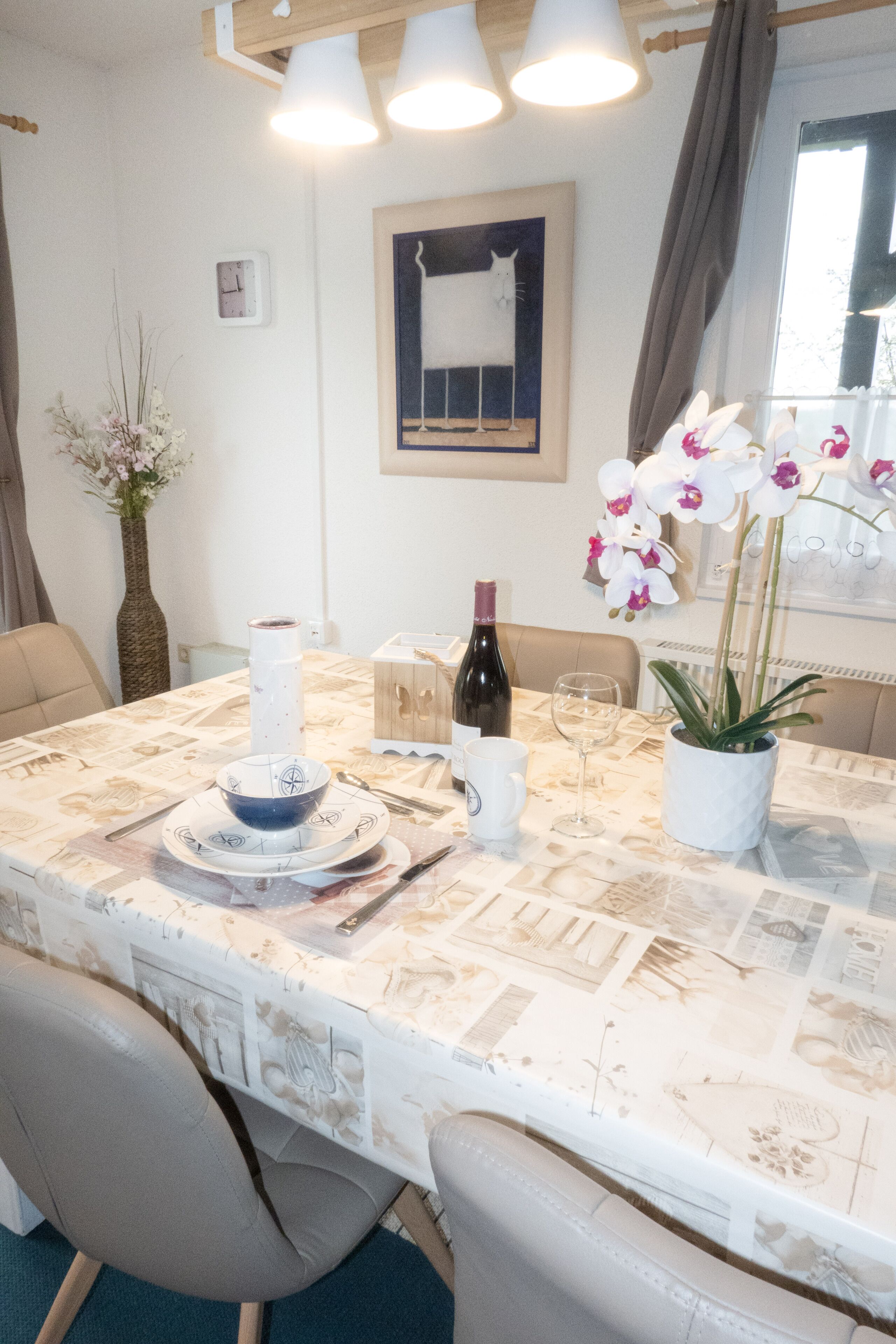A dining area with a table set for two, a vase of orchids, and a bottle of wine.