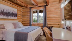 Un dormitorio tipo cabaña de troncos con cama, escritorio, ventana con cortinas y un cuadro en la pared.