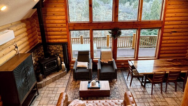 Interior acogedor de una cabaña de madera con un ventanal grande, chimenea, sofá y zona de comedor.