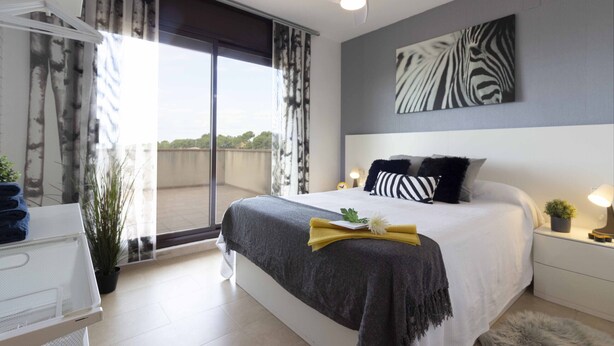Une chambre moderne avec un grand lit, un ventilateur de plafond, une vue à travers une porte coulissante et une œuvre d’art à motifs zébrés accrochée au mur.