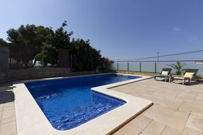 Une piscine rectangulaire dont les bords sont recouverts de carrelage, entourée d’une terrasse également carrelée. On y trouve des chaises longues et une petite table avec une boisson.