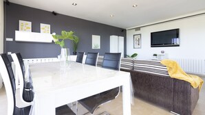 Un salon moderne comprenant une table à manger, des chaises, un canapé, un téléviseur et des œuvres d’art décoratives au mur.