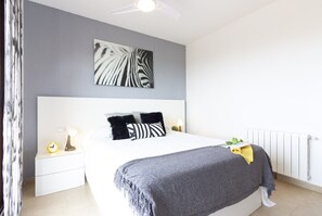 Un dormitorio con cama, mesita de noche, cuadro de cebra colgado en la pared, ventilador de techo y radiador.