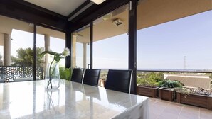 Une table avec un plateau en verre, des chaises, une plante en pot et une vue sur la mer.