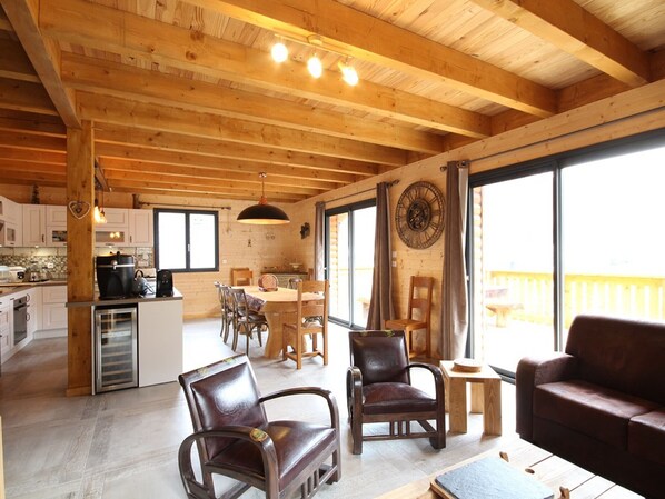 A spacious living area with wooden beams, a dining table, leather chairs, and a sofa.