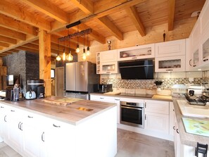 A modern kitchen with wooden beams, a large island, stainless steel appliances, and a tiled backsplash.