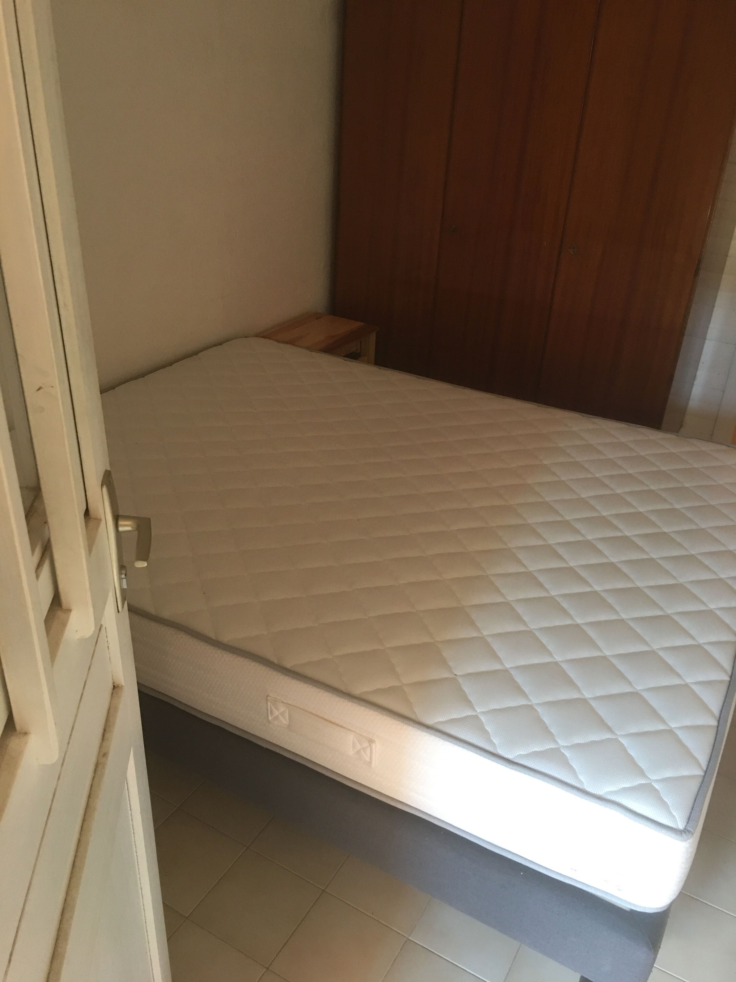 Une pièce comprenant un lit, une armoire en bois et un petit tabouret en bois.