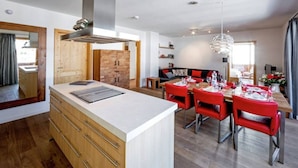 A modern kitchen with a central island, wooden cabinets, and a dining area with red chairs and a table set for four. - Top Location Gerlos! - Lovely Apartment - 6P (Gerlos)