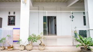 A covered outdoor area with potted plants, a white wall, and a window.