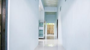A hallway with white walls and a shiny floor, leading to a room with a wooden door and a window.