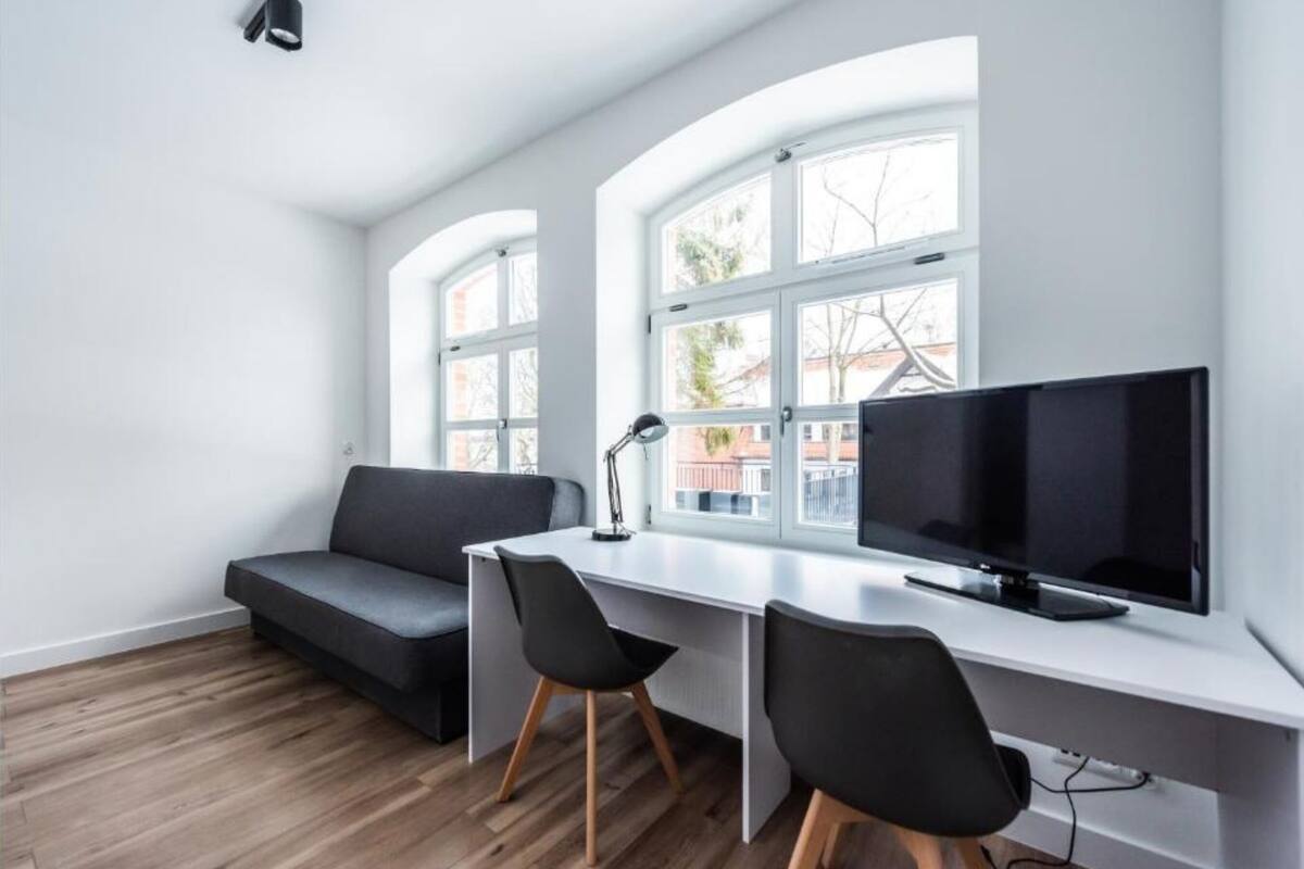 A modern office space with a desk, two chairs, a black sofa, and a large window with multiple panes.