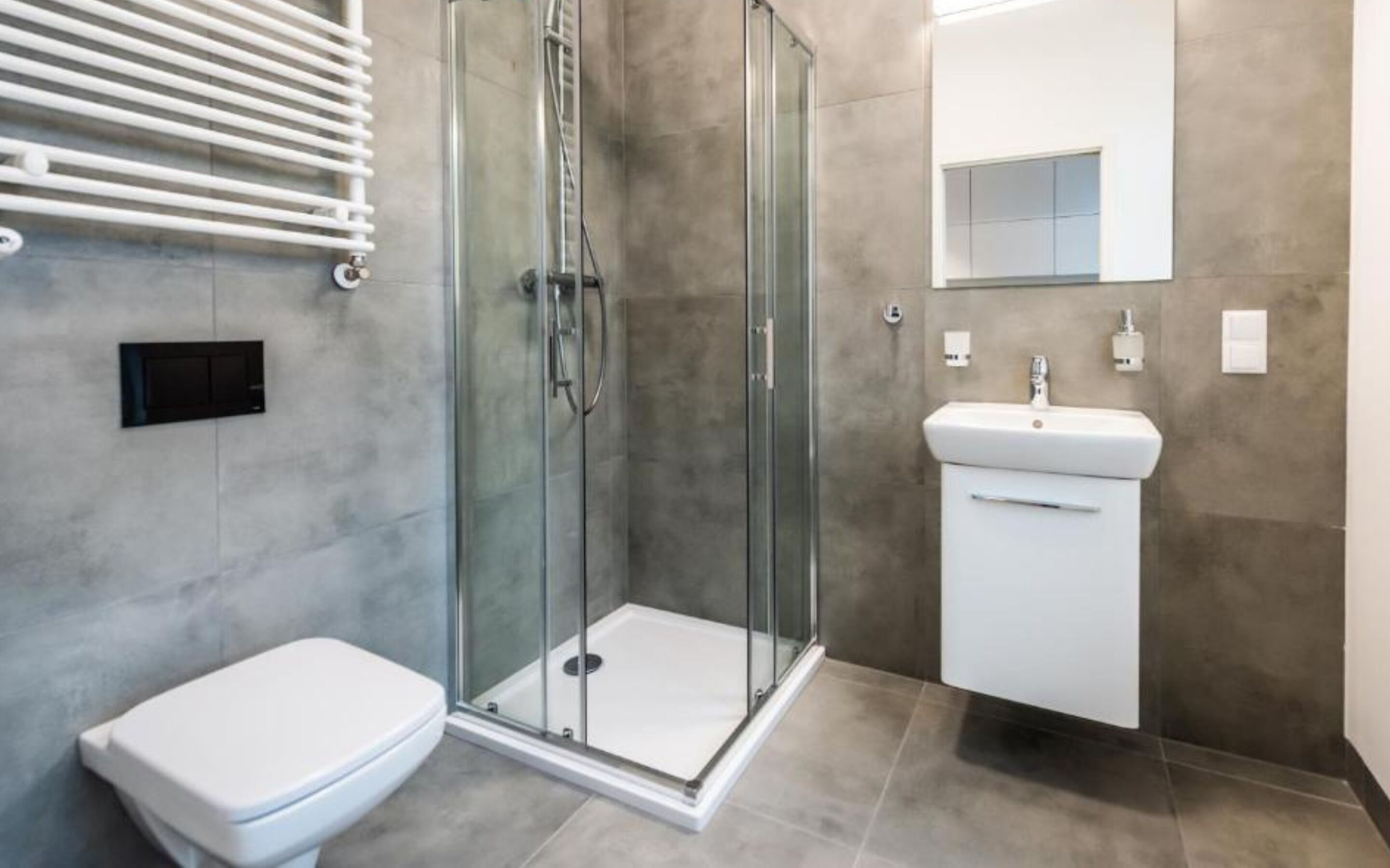 A modern bathroom with a glass-enclosed shower, a white toilet, and a sink with a mirror above it.