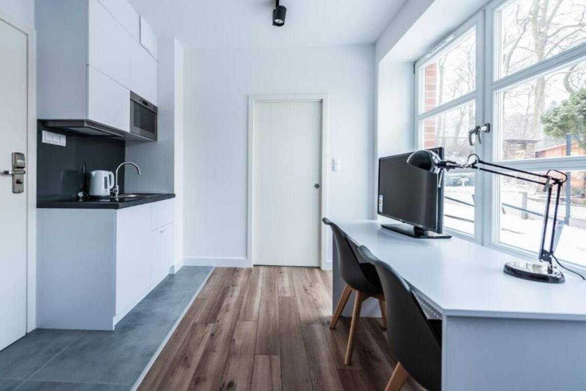 A modern kitchen with a built-in oven, a microwave, and a kettle on the countertop. There is a large window providing natural light and a view of the outside.