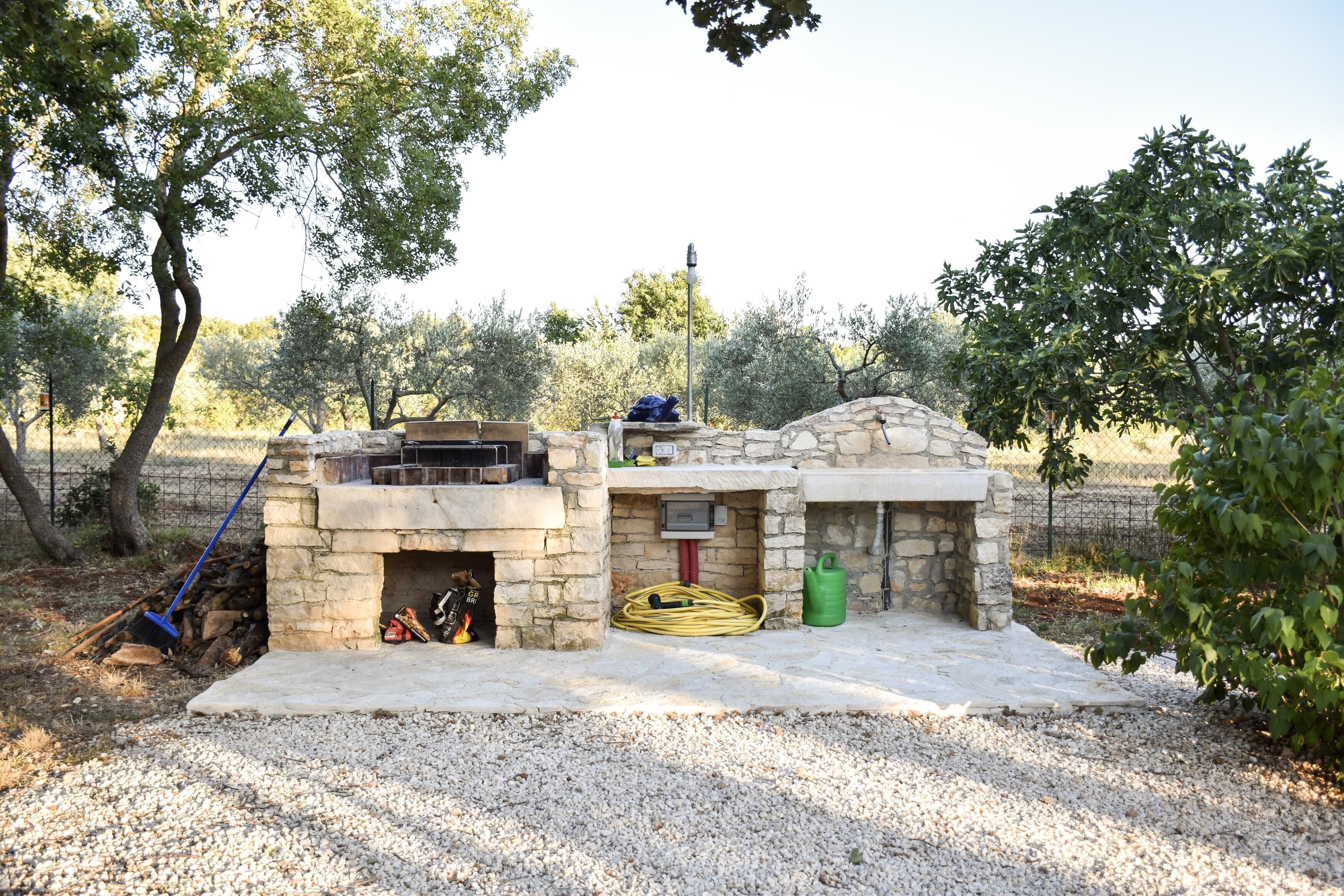 A stone-built outdoor kitchen with a grill, a hose, and a fire pit.