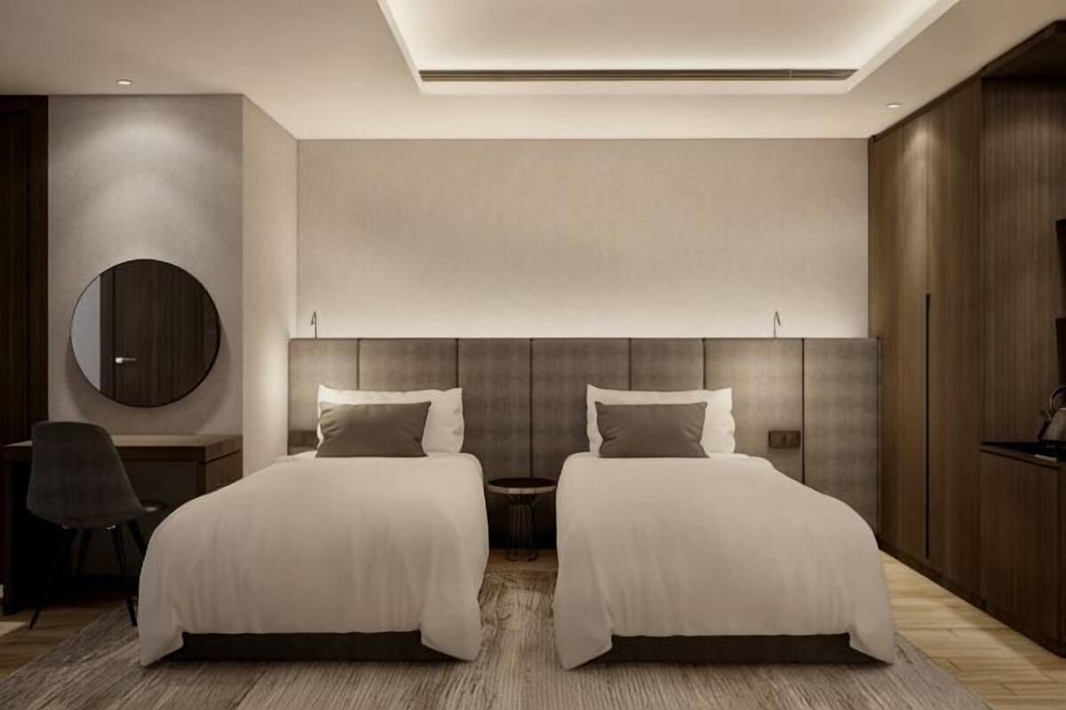 Ein modernes Hotelzimmer mit zwei Betten, einem runden Spiegel, einem Schreibtisch und einem großen Kleiderschrank.