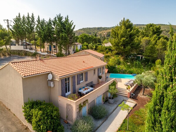 A Mediterranean-style villa with a tiled roof, a swimming pool, and lush greenery.