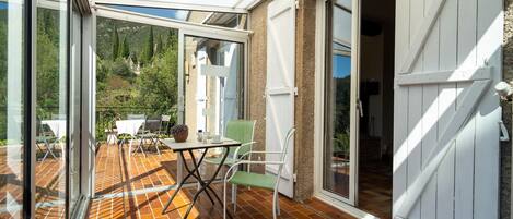 A covered patio with a table and chairs, a sliding glass door, and a view of a mountainous landscape.