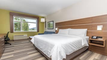 Quarto de hotel moderno com uma cama grande, uma mesa de escritório e uma cadeira. Há uma janela com vista para árvores e montanhas.