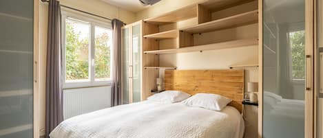 A bedroom with a bed, built-in shelving, a window with curtains, and a radiator.
