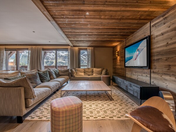 A cozy living room with a sofa set, a coffee table, and a TV mounted on a wooden wall. - Ski-in/Ski-out Duplex with Jacuzzi, Near Shops and ESF, Covered Parking Included (Méribel)