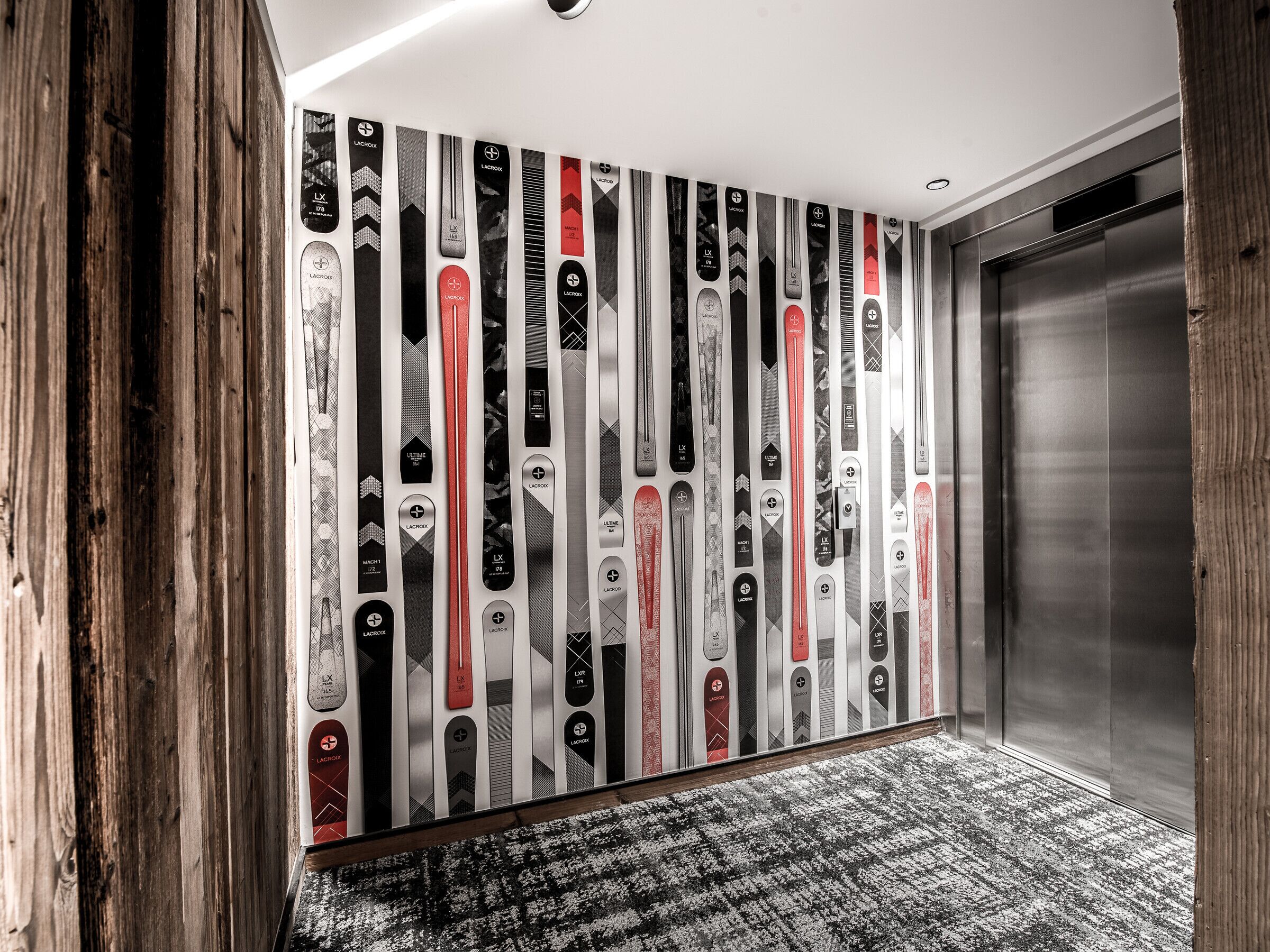 Væg med skitur-tapet, trægulv og en moderne elevator.