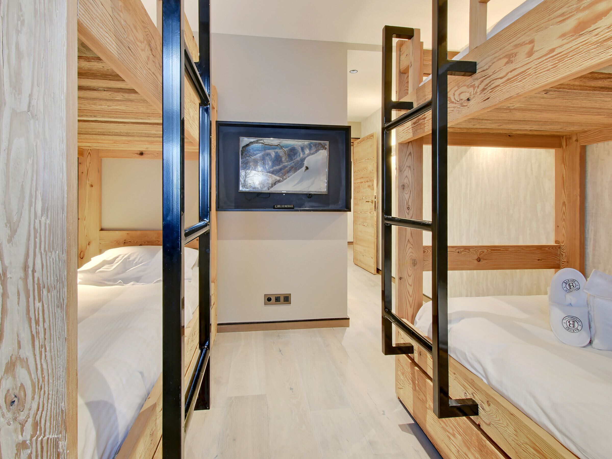 A room with bunk beds, a television mounted on the wall, and a power outlet on the floor.