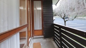 A covered porch with a wooden door and a view of a parking lot and trees.