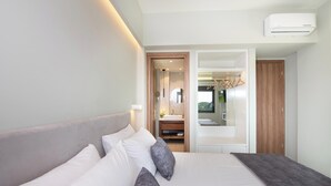 Habitación de hotel moderna con una cama grande, una mesita de noche, un espejo y un baño visible a través de una puerta abierta.