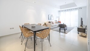 Ein modernes Wohnzimmer mit Essbereich, weißen Wänden und einem großen Fenster mit Vorhängen.