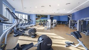 Ein Fitnessstudio mit Laufbändern, Kraftgeräten und einer Wandmalerei, die eine Strandlandschaft zeigt.