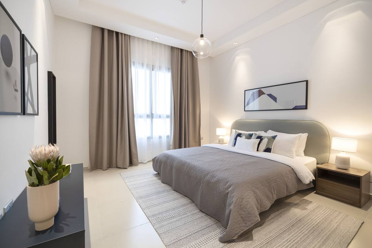 Un dormitorio moderno con una cama grande, mesitas de noche, una lámpara de pie y una ventana con cortinas.