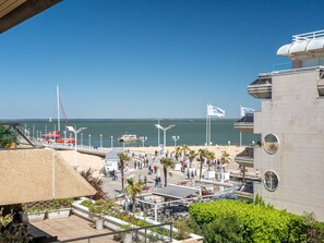 A coastal promenade with a beach, a boat dock, and a modern building with a circular window.