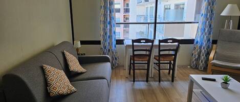 Un saló amb un sofà, dues cadires, una taula petita i una finestra amb cortines estampades.