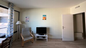 Una habitación con una silla de madera, un televisor sobre un soporte blanco, una puerta y dos carteles en la pared.